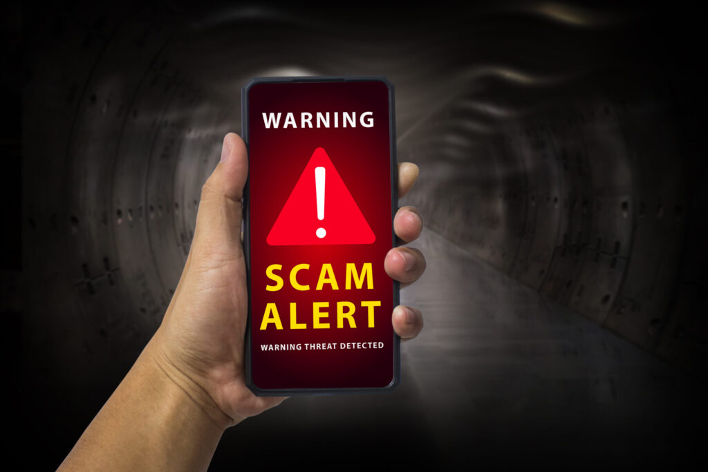 Man hand holding a mobile phone with red screen and warning icon with the text "scam alert", security mobile concept, security risk.